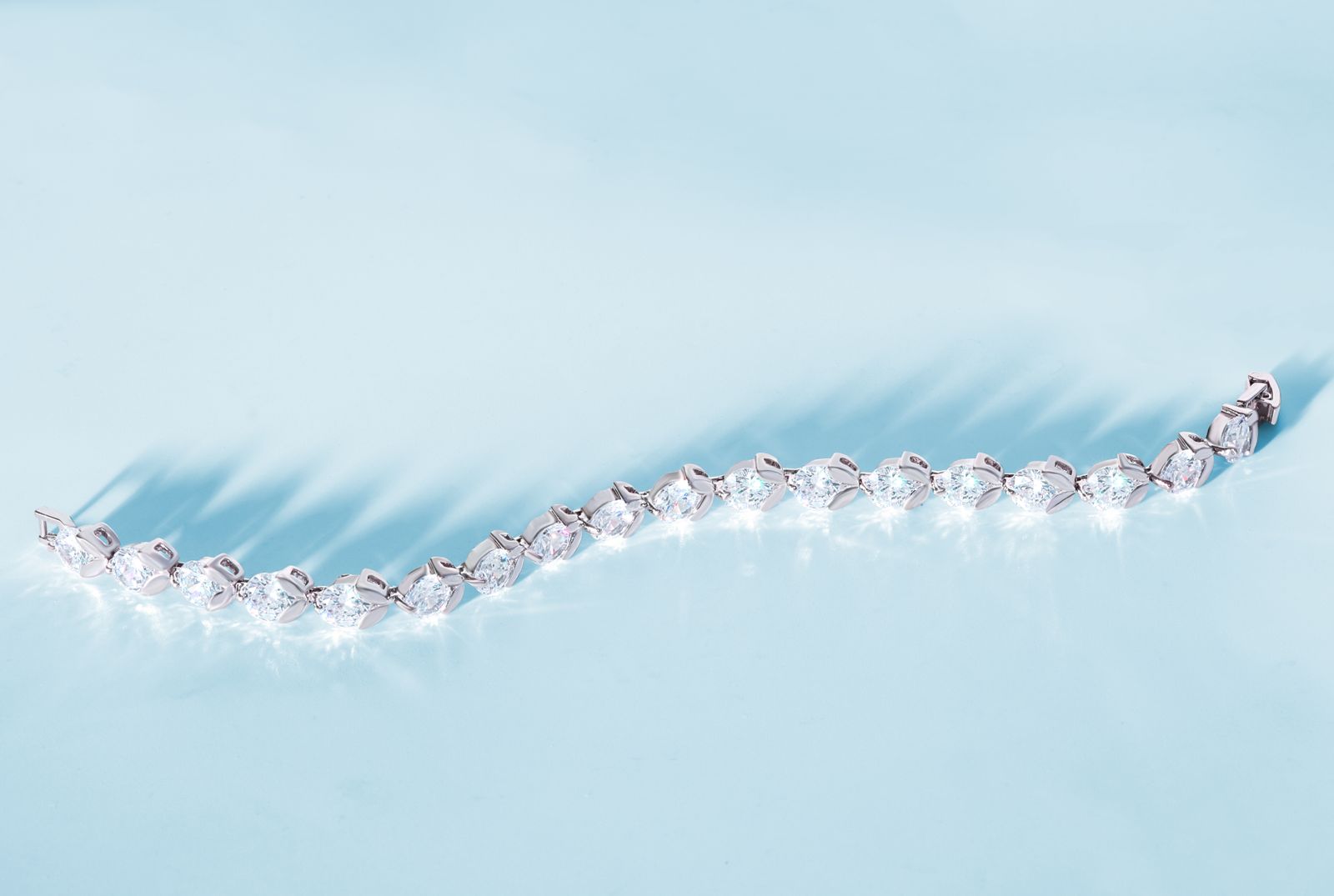 A diamond tennis bracelet with delicate prong settings on a pale studio surface